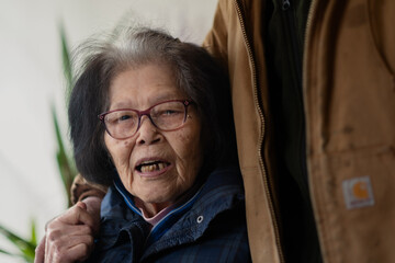An Asian grandmother in her nineties is engaged in conversation while a relative lovingly puts his...