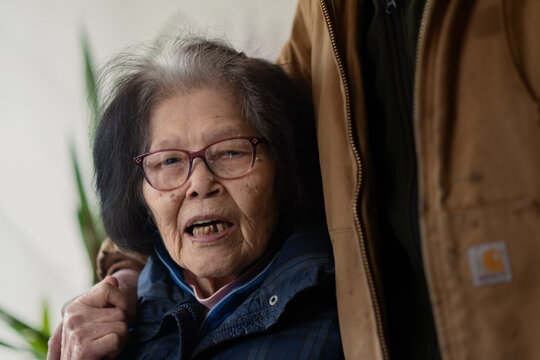 An Asian grandmother in her nineties is engaged in conversation while a relative lovingly puts his arm around her. She is of Okinawan (Ryukyuan) ancestry.