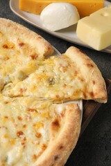Delicious cheese pizza and different kinds of cheese on dark grey table, closeup