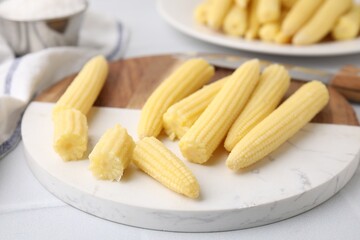 Tasty fresh yellow baby corns and knife on white tiled table, closeup