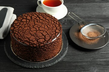 Delicious chocolate truffle cake, cocoa powder and tea on black wooden table - obrazy, fototapety, plakaty