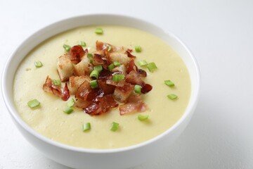 Tasty potato soup with bacon, green onion and croutons in bowl on white table, closeup