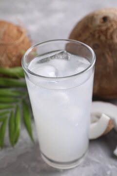 Glass of coconut water with ice cubes, palm leaf and nuts on grey table