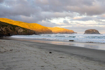 Wundersch&ouml;ner Strand im S&uuml;den von Neuseeland im Sonnenuntergang mit Wellen und Wolken