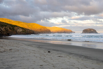 Wunderschöner Strand im Süden von Neuseeland im Sonnenuntergang mit Wellen und Wolken