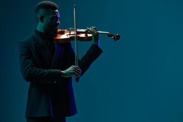 Elegant musician in suit playing violin on dark blue background with dramatic lighting and shadows