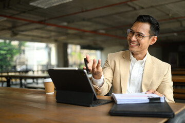 Portrait of smiling businessman sitting at a cafeteria and working with his laptop