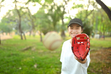 Joyful asian girl in leather glove playing baseball on green grassy lawn during summer day