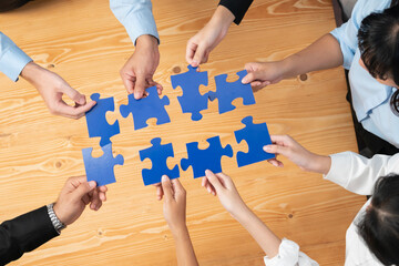 Top view multiethnic business people holding jigsaw pieces and merge them together as effective...