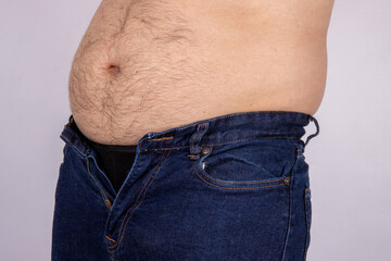 A middle aged slightly over weight man, trying to put on a pair of jeans but they wont fasten due...