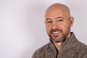 A middle aged bald shaven headed man with a beard wearing a jumper on white background
