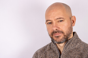 A middle aged bald shaven headed man with a beard wearing a jumper on white background