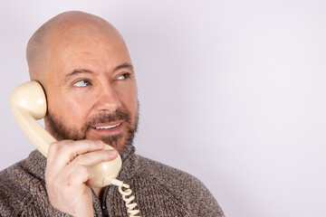 A middle aged man wearing a jumper smiling using a retro style telephone a white background