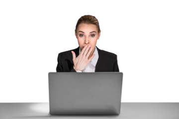 A surprised businesswoman covering her mouth, sitting behind a laptop on a white background, expressing shock