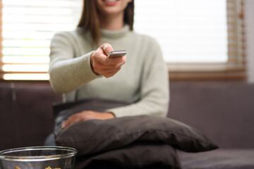 Young woman with remote control watching television on sofa at home.
