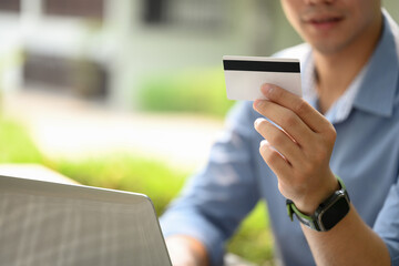 Satisfied young man holding credit card making purchase or payments on laptop computer