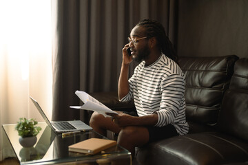 African American businessman talking on mobile phone and working with laptop at home