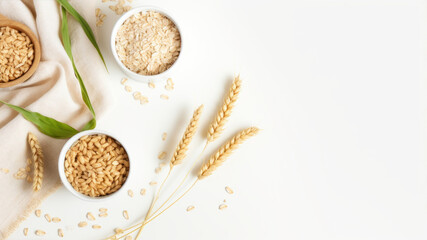 Fototapeta na wymiar Oat flakes in bowls and ears of wheat on white background. Flat lay, top view.
