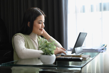 Young businesswoman sitting in modern living room and working with laptop. Remote work concept