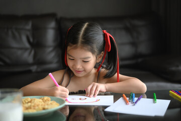 Cute young Asian girl drawing with colored pencil in living room