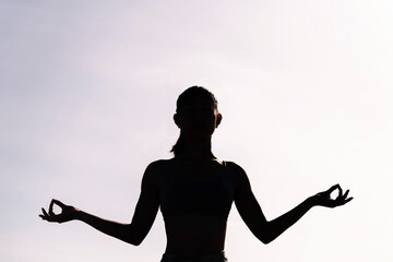 backlight of young woman doing yoga meditation, concept of mental relaxation and healthy lifestyle