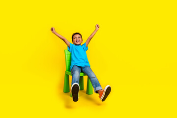 Full body photo of mixed race child dressed blue t-shirt hands up sit on chair look empty space isolated on vibrant yellow background