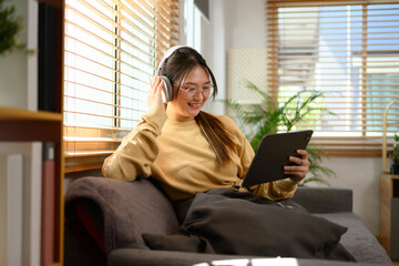 Cheerful teenage asian girl wearing headphone watching video on digital tablet