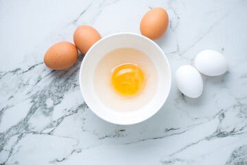 Bowl with uncooked goose egg and raw chicken eggs on a white marble background, horizontal shot...