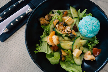 Blue rice and salad with vegetables and seafood. Green salad in dark bowl with cutlery. Thai...