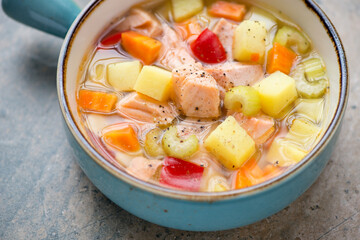 Vegetable soup with salmon fillet in a turquoise serving bowl, middle closeup, selective focus, horizontal shot