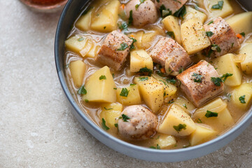 Dublin coddle or Irish traditional sausage and potato stew, horizontal shot on a beige stone background, middle close-up