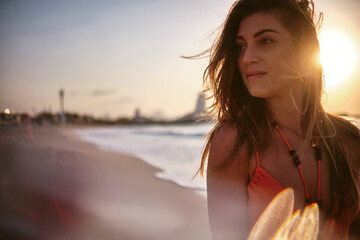 Close-up of an attractive woman smiling gently with sunset lighting beach in the background