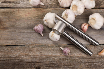 Garlic press and bulbs on wooden table, flat lay. Space for text