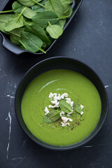 Bowl of freshly made spinach cream-soup on a black marble background, vertical shot, high angle view