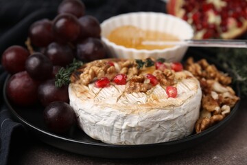Plate with tasty baked camembert, honey, grapes, walnuts and pomegranate seeds on table, closeup
