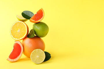 Fresh ripe citrus fruits and green leaves on yellow background, space for text