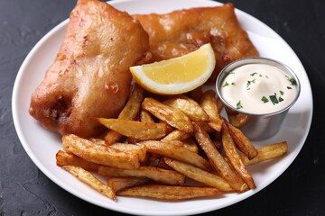 Tasty fish, chips, lemon and sauce on black table, closeup