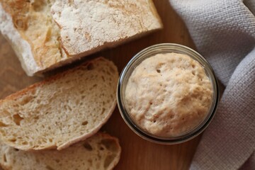 Sourdough starter in glass jar and bread on wooden table, top view