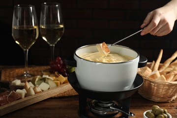 Woman dipping piece of bread into fondue pot with melted cheese at wooden table, closeup