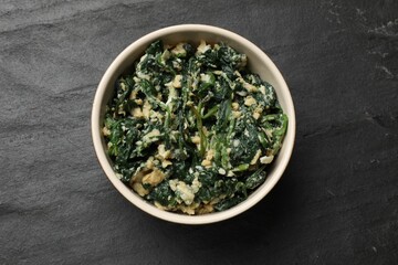 Tasty spinach dip with egg in bowl on black table, top view