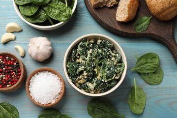 Tasty spinach dip with egg in bowl, bread and spices on light blue wooden table, flat lay