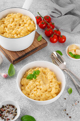 Mac and cheese in a white bowl with fresh basil on top on a gray concrete background. American cuisine, comfort food. Copy space.