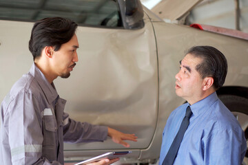 Auto technician talking and explaining about repairing progress to client in garage.