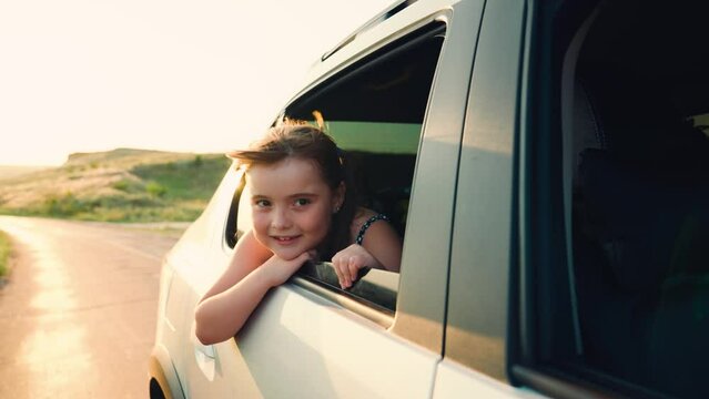 child girl face looks smiling from car out window, free girl waving her hand from window, beautiful little girl stuck out hand from car window, hand, wind freedom from window sunset, child smile