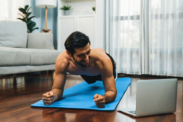 Athletic and sporty man doing plank on fitness mat during online body workout exercise session for fit physique and healthy sport lifestyle at home. Gaiety home exercise workout training.