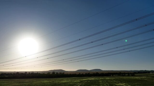 Drone flying past powerlines in a sunset field
