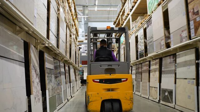 Warehouse worker with forklift rides in tile store
