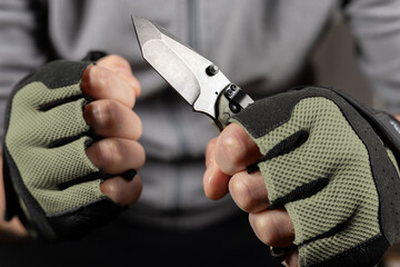 The man wearing tactical gloves using folding knife - obrazy, fototapety, plakaty