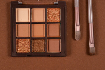 Two cosmetic brushes with light brown eye shadow dust sitting on top of palette of pale nude eye shadow shades