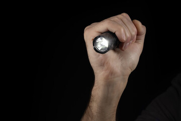 Black flashlight in human hands on a black background, including a white beam